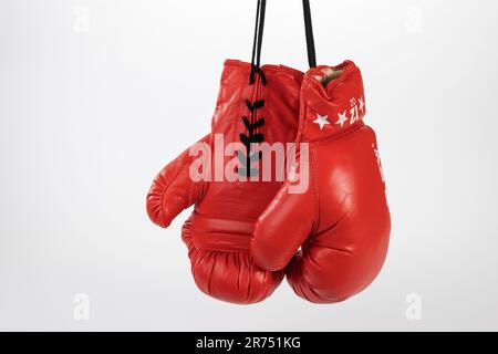 Paio di guanti da boxe rossi appesi su pizzo, fondo bianco, Foto Stock