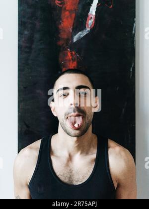 Uomo, capelli corti, barba di tre giorni, maglietta muscolare, bastone lingua, pillola, mezzo ritratto Foto Stock
