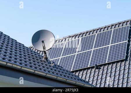 Frammento del tetto di un edificio residenziale con pannelli solari installati e un'antenna parabolica. Cielo blu chiaro. Foto Stock