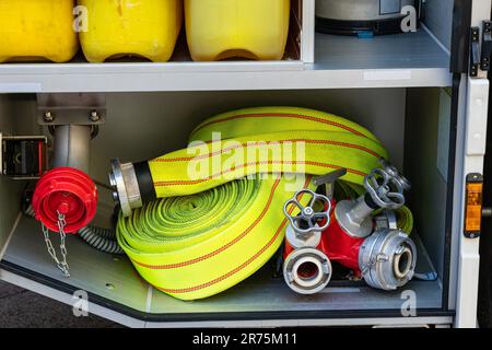 Tubo antincendio giallo arrotolato e sdoppiatore d'acqua con valvole in una pista antincendio. Primo piano. Foto Stock