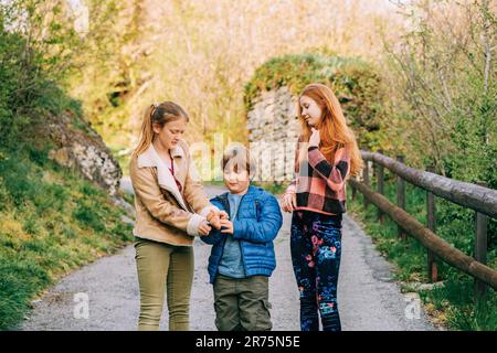 Gruppo di 3 bambini divertenti che giocano insieme in campagna, moda primaverile per bambini Foto Stock