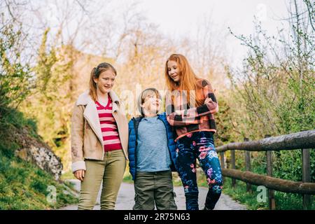 Gruppo di 3 bambini divertenti che giocano insieme in campagna, moda primaverile per bambini Foto Stock