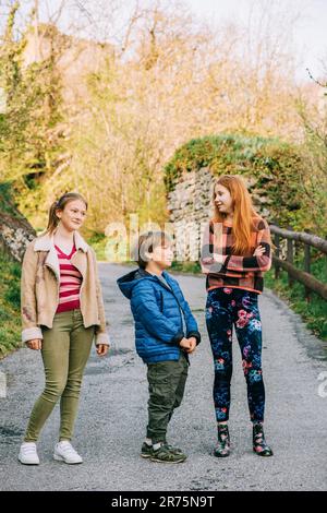 Gruppo di 3 bambini divertenti che giocano insieme in campagna, moda primaverile per bambini Foto Stock