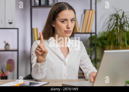 La giovane donna di affari caucasica che lavora sul computer portatile scuote il dito, dicendo No fate attenzione a scossare e dare consigli per evitare pericolo errore disapprovazione segno in ufficio. Fidata ragazza freelance Foto Stock