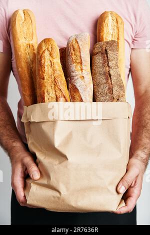 L'uomo tiene pani freschi di baguette di pane in sacchetto di carta su sfondo chiaro. Panetteria, concetto di cibo Foto Stock
