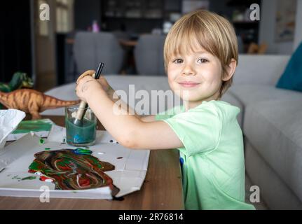 Giovane ragazzo dipingendo scritta verde decorativa su un sketchpad con un pennello e vernice color acqua Foto Stock