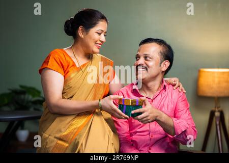 Donna indiana felice che dà dono al marito a casa - concetto di anniversario di matrimonio, la convivenza e l'affetto Foto Stock