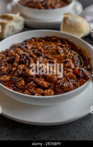 Stufato con fagioli, al forno, fagioli, carne di pollo e verdure su un piatto con cucchiaio Foto Stock