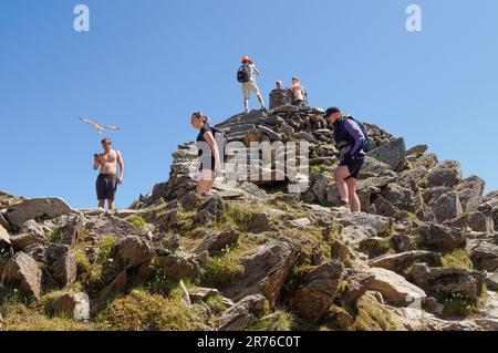 Escursionisti che scattano fotografie e si godono una pausa in una calda giornata estiva in cima allo Snowdon Yr Wyddfa nel Parco Nazionale di Eryri, Galles del Nord, Regno Unito Foto Stock