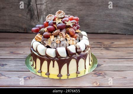 Torta autunnale al cioccolato e decorata con uva, noci, tartufi al cioccolato, marshmallow e stelle. Sfondo rustico, cibo comfort Foto Stock