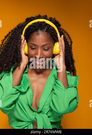 Gli occhi di una donna afro-americana si sono chiusi mentre teneva le cuffie per ascoltare la sua musica preferita Foto Stock