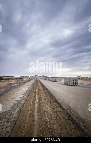 Strada diritta con terra scavata per l'installazione di cavi di comunicazione e sensori di sicurezza su binari ferroviari sotto cielo nuvoloso e cupo Foto Stock