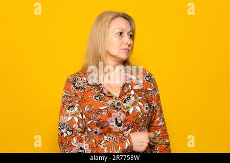 Ritratto di una donna caucasica bionda nel suo 40s con un serio volto malinconico guardando al lato con pietà, isolato su sfondo giallo studio. Foto Stock