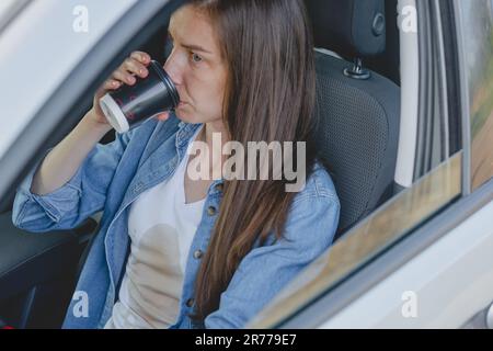 Donna che si versa caffè o tè su se stessa durante la guida di un'auto. Macchie di caffè sporche. Vestiti rovinati. Foto Stock