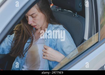 Donna che si versa caffè o tè su se stessa durante la guida di un'auto. Macchie di caffè sporche. Vestiti rovinati. concetto di colorazione della vita quotidiana Foto Stock