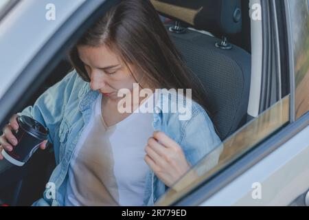 Donna che si versa caffè o tè su se stessa durante la guida di un'auto. Macchie di caffè sporche. Vestiti rovinati. concetto di colorazione della vita quotidiana Foto Stock