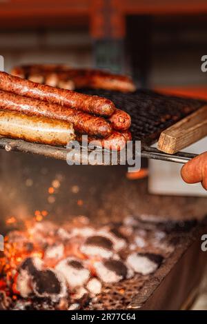 Preparazione di succosa salsiccia di manzo e bradwurst alla griglia con carbone caldo e incandescente alla fine della giornata nel fine settimana Foto Stock