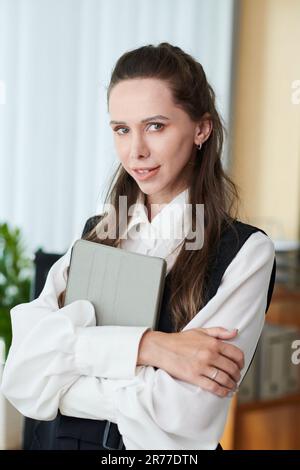 Immagine verticale di un giovane manager con un tablet che sorride davanti alla fotocamera in ufficio Foto Stock