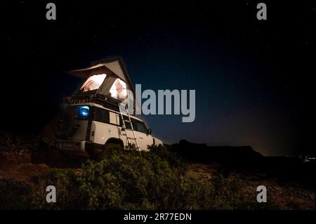 Romantico campeggio in una tenda sul tetto su un veicolo fuoristrada 4x4 di notte sotto le stelle Foto Stock