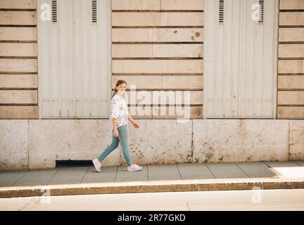 Bambina che cammina per le strade della città, indossa una blusa, pantaloni blu e sneaker rosa Foto Stock