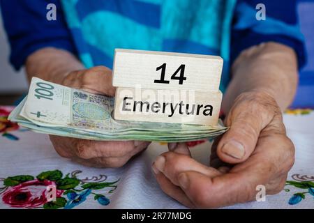 Il pensionato polacco detiene denaro e blocchi di legno con l'iscrizione "14 pensione" in polacco. Concetto sociale. Pensioni supplementari 13th e 14th per seni Foto Stock
