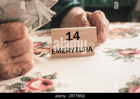 Il pensionato polacco detiene denaro e blocchi di legno con l'iscrizione "14 pensione" in polacco. Concetto sociale. Pensioni supplementari 13th e 14th per seni Foto Stock