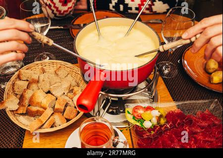 Gli amici mangiano fonduta di formaggio in un accogliente ristorante tradizionale svizzero Foto Stock