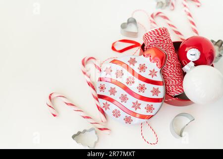 Le caramelle di Natale, insieme ai taglierini dei biscotti, ai giocattoli dell'albero di Natale ed al filo rosso per il rivestimento del regalo, si trovano su un tavolo bianco. Messa a fuoco selettiva, rumore. CHRI Foto Stock