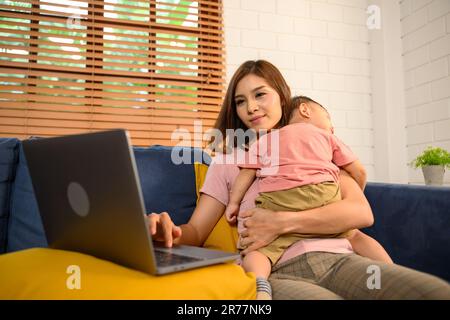 mamma che usa il notebook durante il sonno del bambino nel salotto. Foto Stock