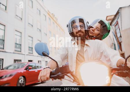 Felice giovane coppia con cappelli protettivi sta guidando su uno scooter d'epoca nella strada di Lisbona Foto Stock
