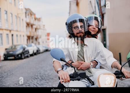 Una felice coppia di turisti con cappelli protettivi sta viaggiando su uno scooter d'epoca a noleggio nella strada di Lisbona Foto Stock
