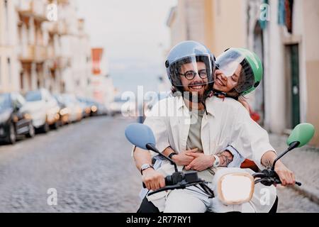 Felice giovane coppia con cappelli protettivi sta guidando su uno scooter d'epoca nella strada di Lisbona Foto Stock