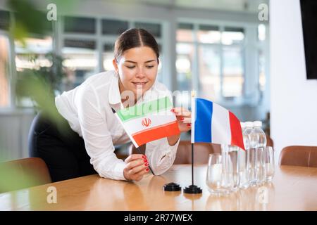 Giovane donna che mette bandiere di Iran e Francia sul tavolo in carica Foto Stock