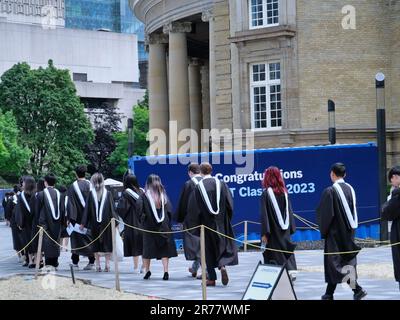 Una processione di studenti universitari laureati in abiti accademici formali va a ricevere i loro diplomi Foto Stock
