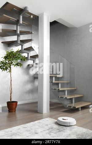 Una scala con scale in legno e un'elegante recinzione in vetro, una colonna di vetro opaco, grande fiore interno nel moderno interno dell'appartamento. Foto Stock