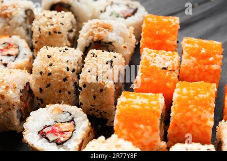 Set di sushi con salmone, tonno, caviale, semi di sesamo su un piatto di ardesia di pietra nera, primo piano. Foto Stock