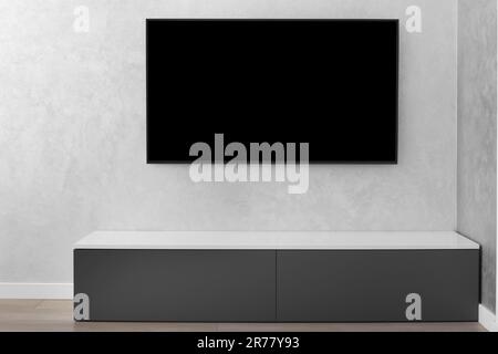 Parte dell'interno di un moderno soggiorno, una Smart TV LED su una parete grigia, un armadietto grigio, un tappeto. Minimalismo negli interni. Foto Stock