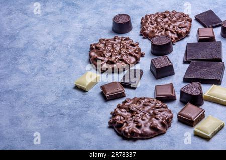 Varietà di prodotti di cioccolato fotografati in studio su sfondo grigio chiaro con texture bianca. Cioccolato fondente, cioccolato al latte, cioccolato bianco, c Foto Stock