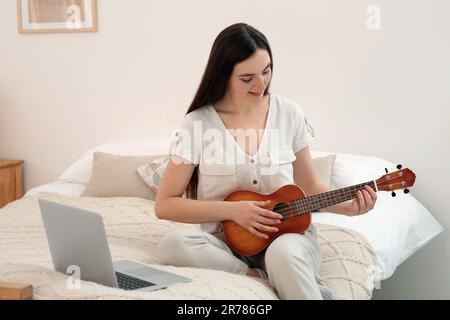 Donna che impara a giocare ukulele con corso di musica online a casa. Tempo per hobby Foto Stock