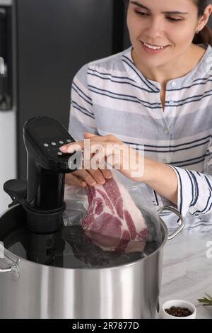 Donna che mette carne confezionata sottovuoto in pentola e utilizzando il circolatore a immersione termica. Cucina sous vide Foto Stock