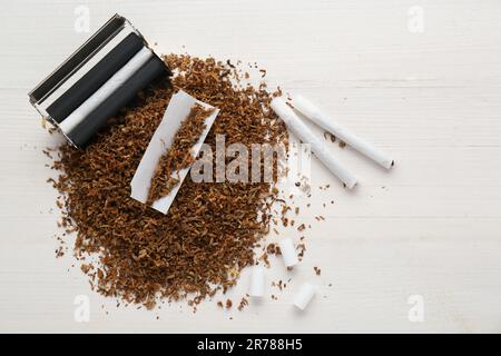 Composizione piatta con rullo e tabacco su tavolo di legno bianco, spazio per testo. Fare le sigarette arrotolate a mano Foto Stock