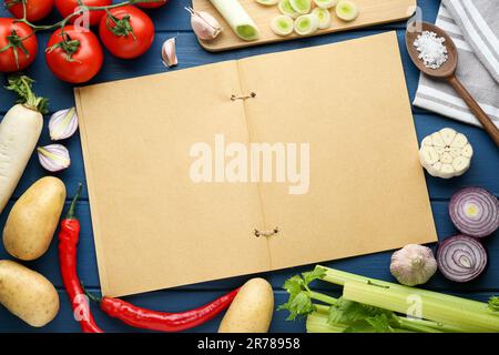 Libro di ricette vuoto circondato da diversi ingredienti su tavola di legno blu, piatto. Spazio per il testo Foto Stock