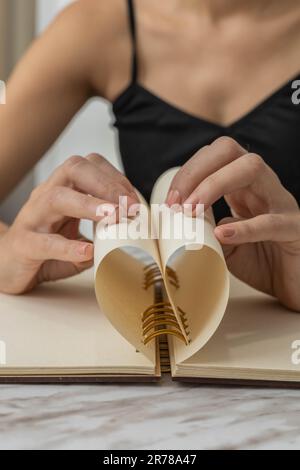 piegare il foglio di carta da un taccuino formando un cuore, eseguendo origami, attività creativa e artistica, dettagli di oggetti di cancelleria Foto Stock