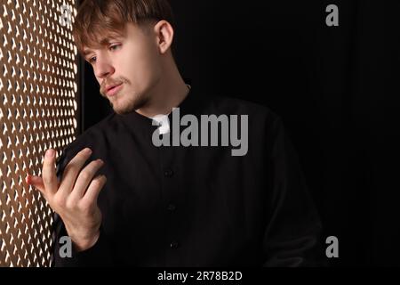 Sacerdote cattolico che parla con il parrocchiano nello stand confessionale Foto Stock