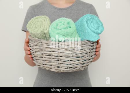 Donna che tiene il cestino di vimini con i tovaglioli morbidi rotolati del terry su fondo chiaro, primo piano Foto Stock