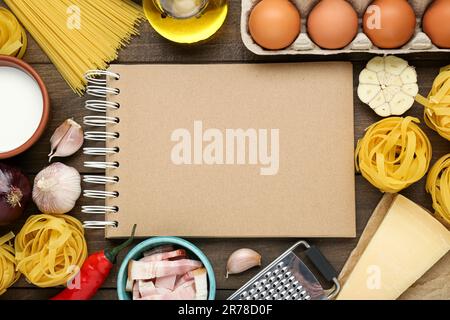 Libro di ricette in bianco circondato da diversi ingredienti su tavolo di legno, piatto. Spazio per il testo Foto Stock