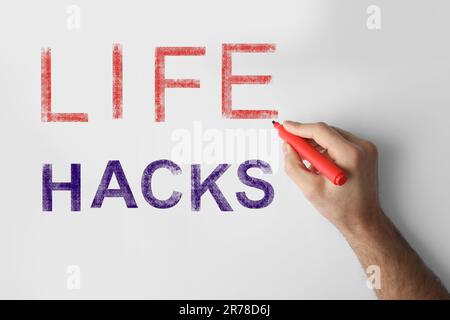 Uomo scrivere parole Life Hacks con marker su lavagna bianca, primo piano Foto Stock