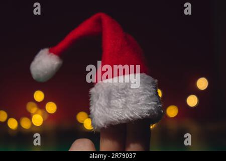 Dita vestite con cappelli rosso-bianco di Babbo Natale. Due dita felici che rappresentano il social network su sfondo rosso. Le dita si affacciano sui cappelli di Santa su sfondo rosso. Felice famiglia che celebra il concetto per Natale o Capodanno. Coppia di dita Foto Stock