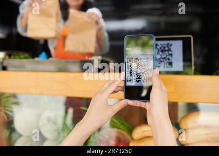Mani di una giovane cliente che scannerizza il codice qr dei prodotti sullo smartphone mentre acquista un fast food da asporto in camion Foto Stock