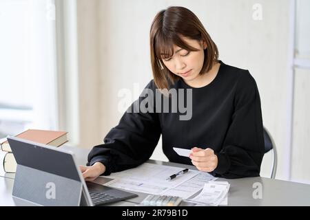 Donna asiatica che inserisce le spese nel software di contabilità Foto Stock